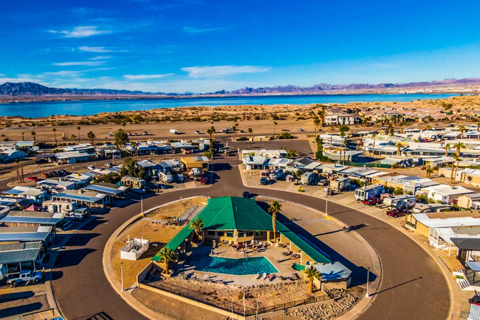 An aerial view of a campground with RVs, a central pool area, and a desert landscape in the background.