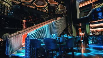 A modern bar area with a unique geometric light design on the ceiling, a staircase with illuminated steps, and bar seating.