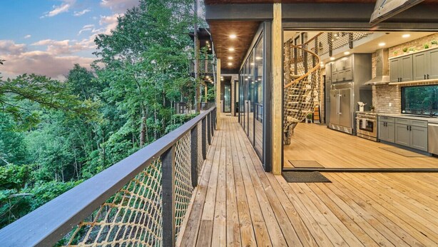 Eine Holzterrasse mit Glasgeländer, das auf einen bewaldeten Bereich blickt.