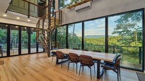 Ein geräumiges Zimmer mit einem großen Holztisch und Stühlen, einer Wendeltreppe und großen Fenstern mit Blick ins Freie.