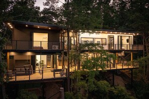 A two-story cabin with a balcony, built into a hillside with a forest backdrop. - Skyview Treehouse- luxury with breathtaking views (Sevierville)