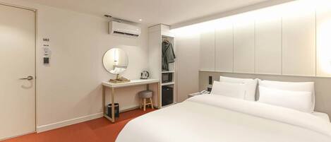 A hotel room with a bed, a desk with a chair, a mirror, an air conditioning unit, and a wardrobe.