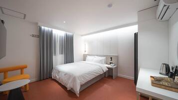 A hotel room with a bed, bedside table, and a small desk with a kettle.
