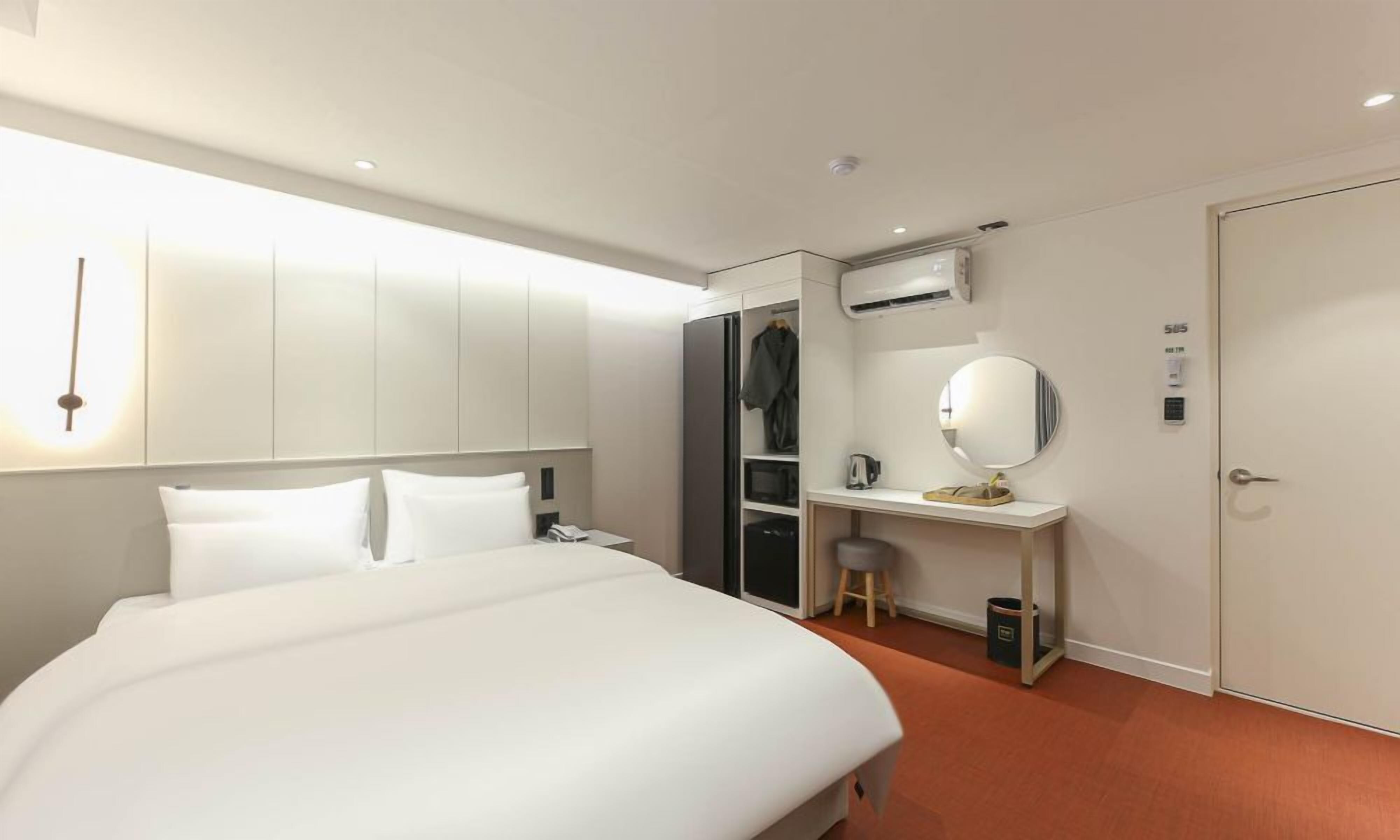 Et hotelværelse med en seng, et skrivebord med et spejl, et garderobeskab og en aircondition.
