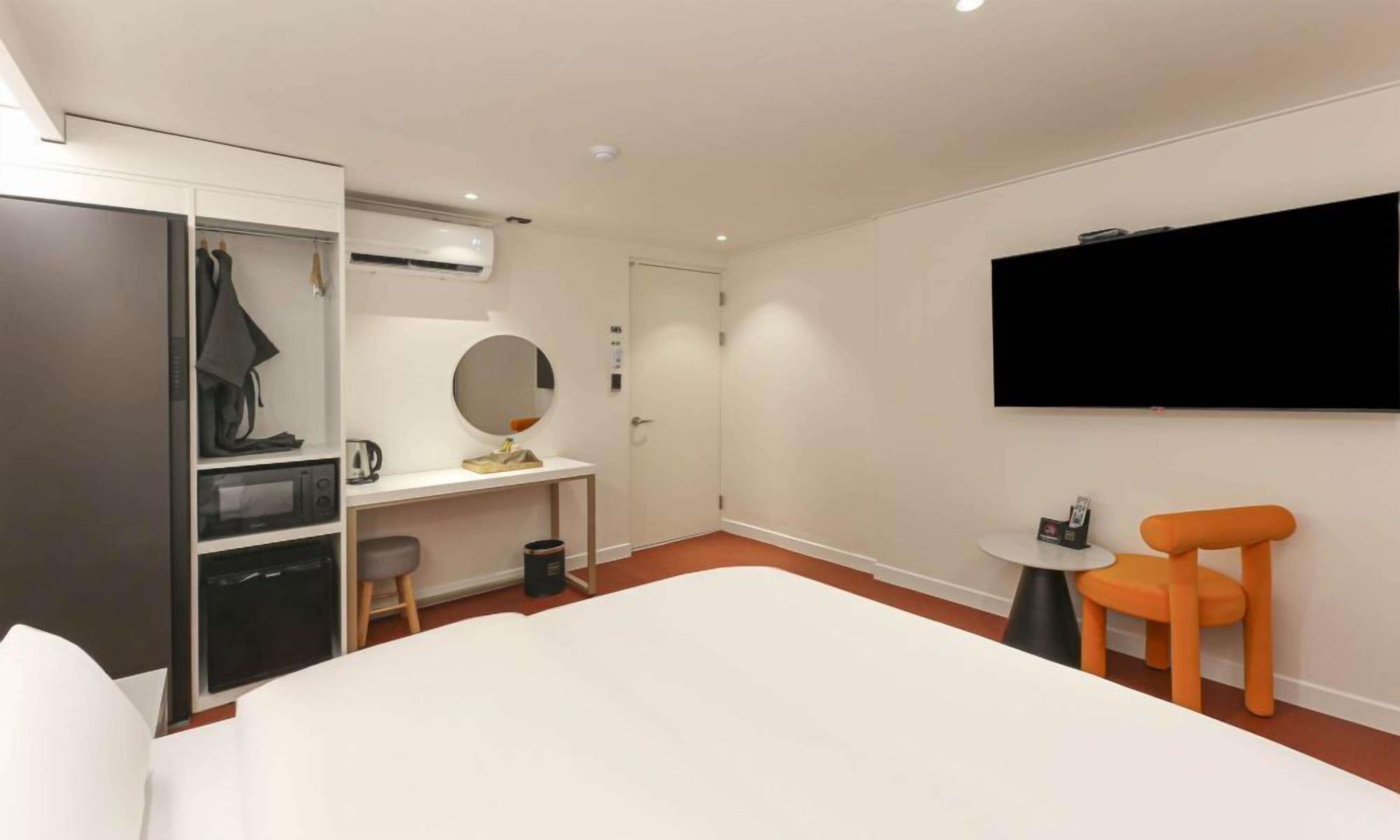 Una habitación de hotel con cama, escritorio, silla, televisión y armario.
