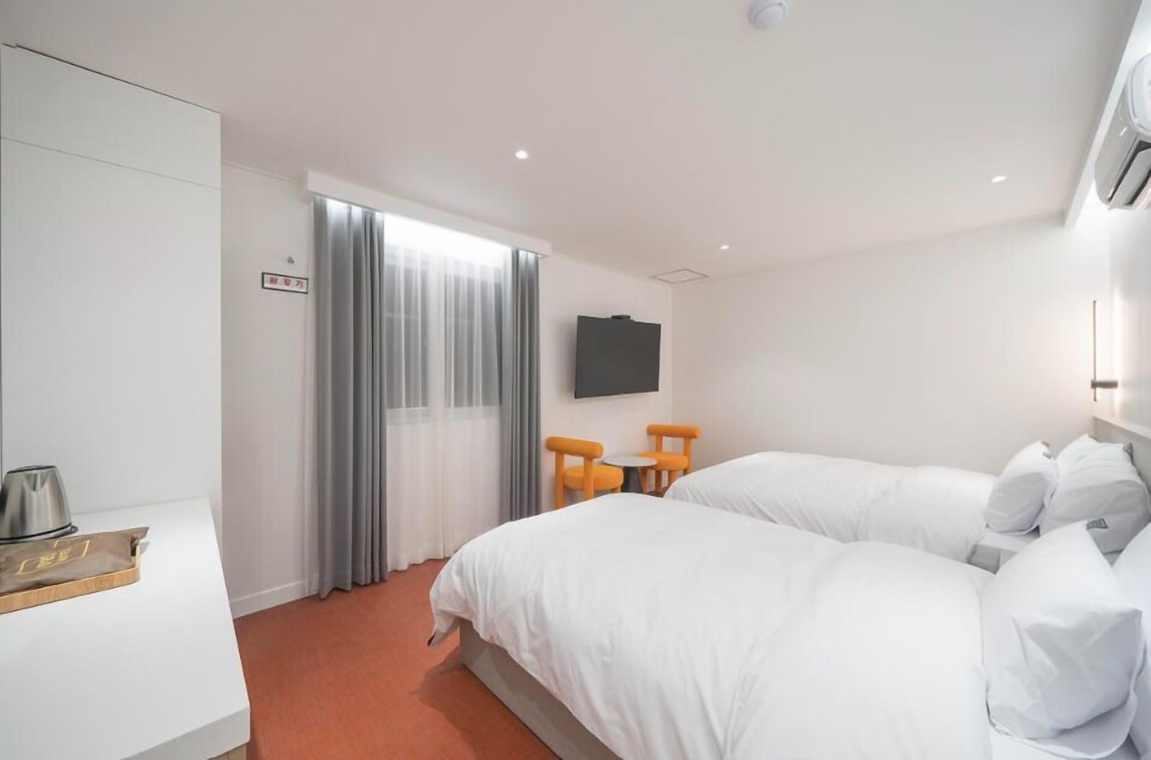 A hotel room with two beds, a desk, a chair, and a TV on the wall.