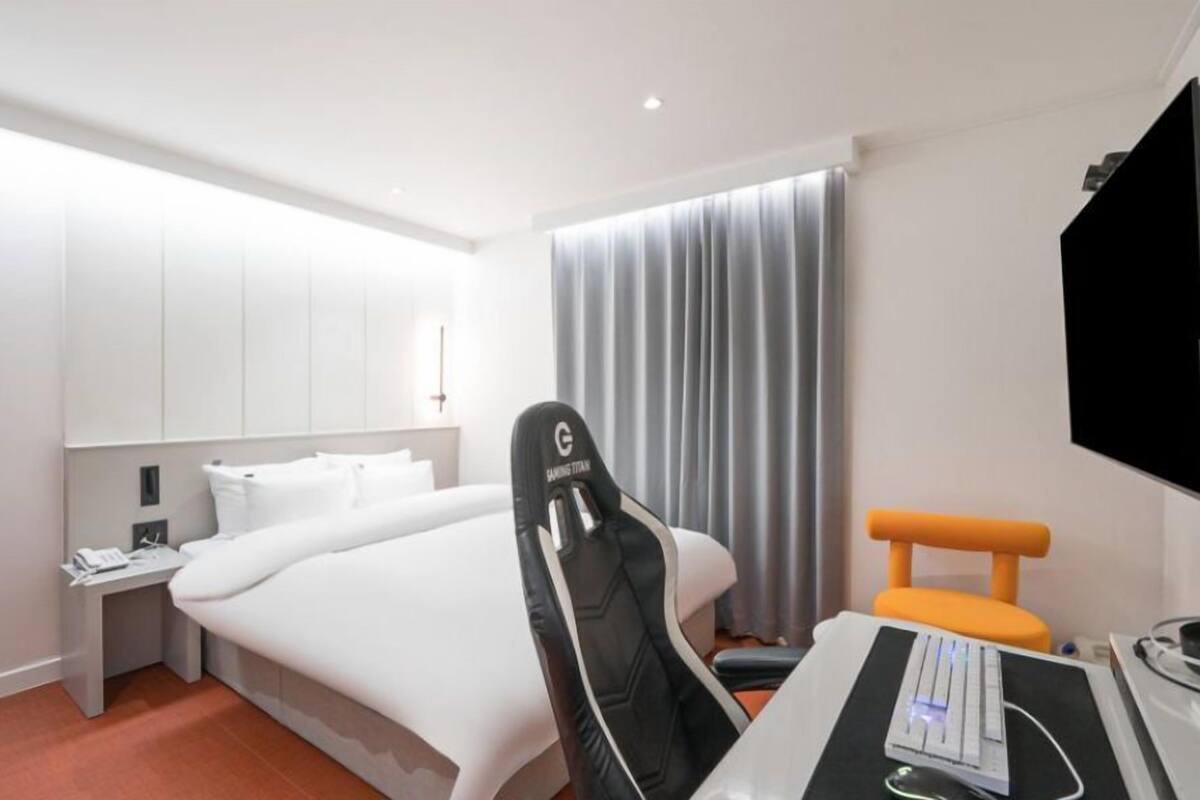 Ein Hotelzimmer mit einem Bett, einem Schreibtisch mit Computer, einem Sessel, einem Fernseher und einem Fenster mit Vorhängen.