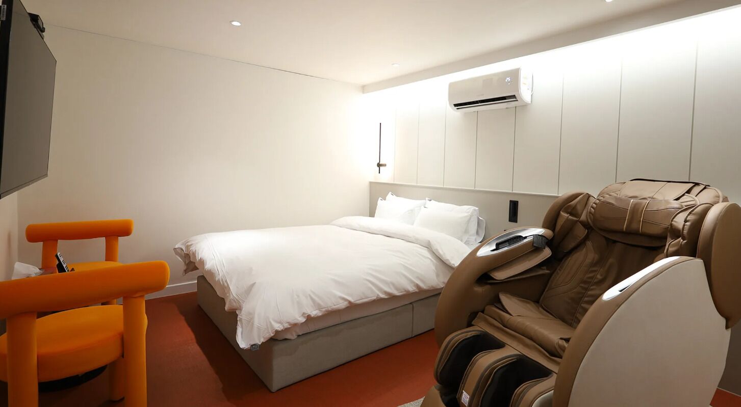 A hotel room with a bed, a massage chair, and a TV.