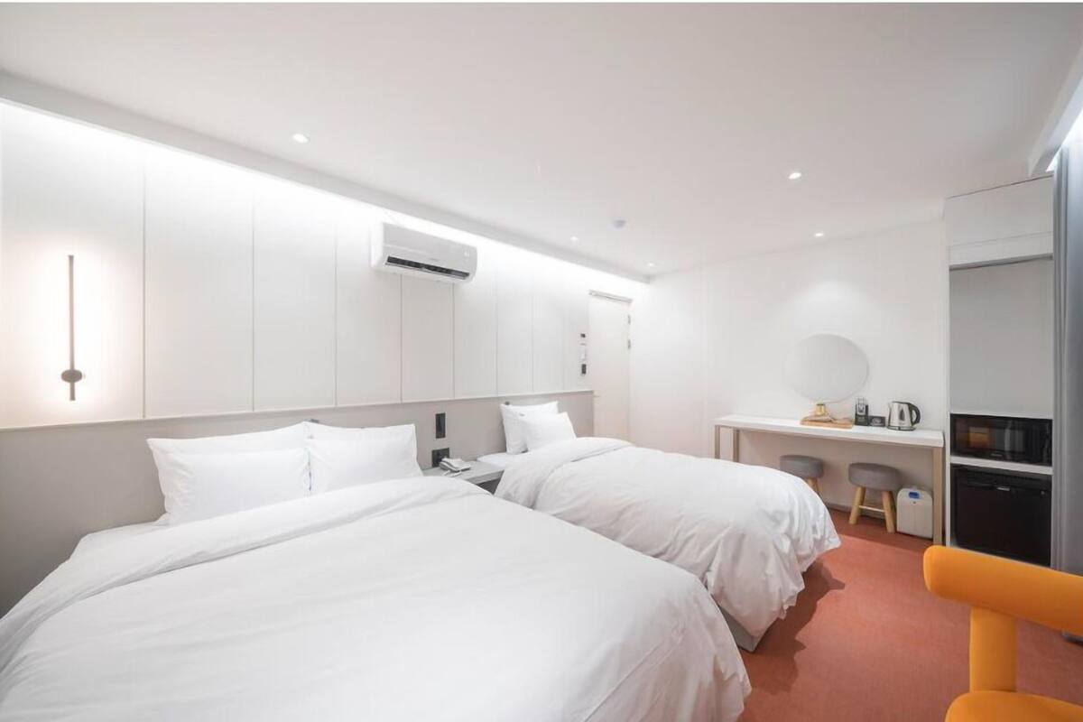 Ein modernes Hotelzimmer mit zwei Betten, einem Schreibtisch, einem Stuhl und einer kleinen Küchenzeile.