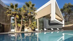 A modern house with a swimming pool, palm trees, and a clear blue sky.