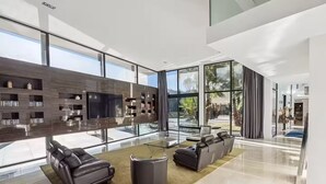 A modern living room with a large TV, leather sofas, and a glass wall overlooking a garden.