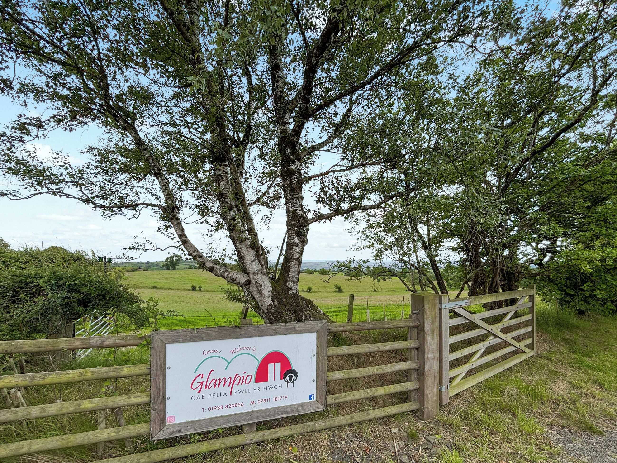 A wooden gate with a sign welcoming visitors to Glampio, including contact information and social media icons.
