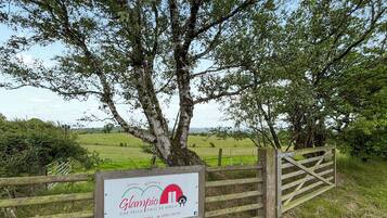 A wooden gate with a sign welcoming visitors to Glampio, including contact information and social media icons.
