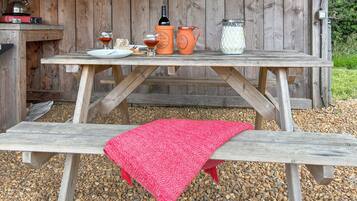 A wooden picnic table with a red blanket, a bottle of wine, glasses, and a jug of milk.