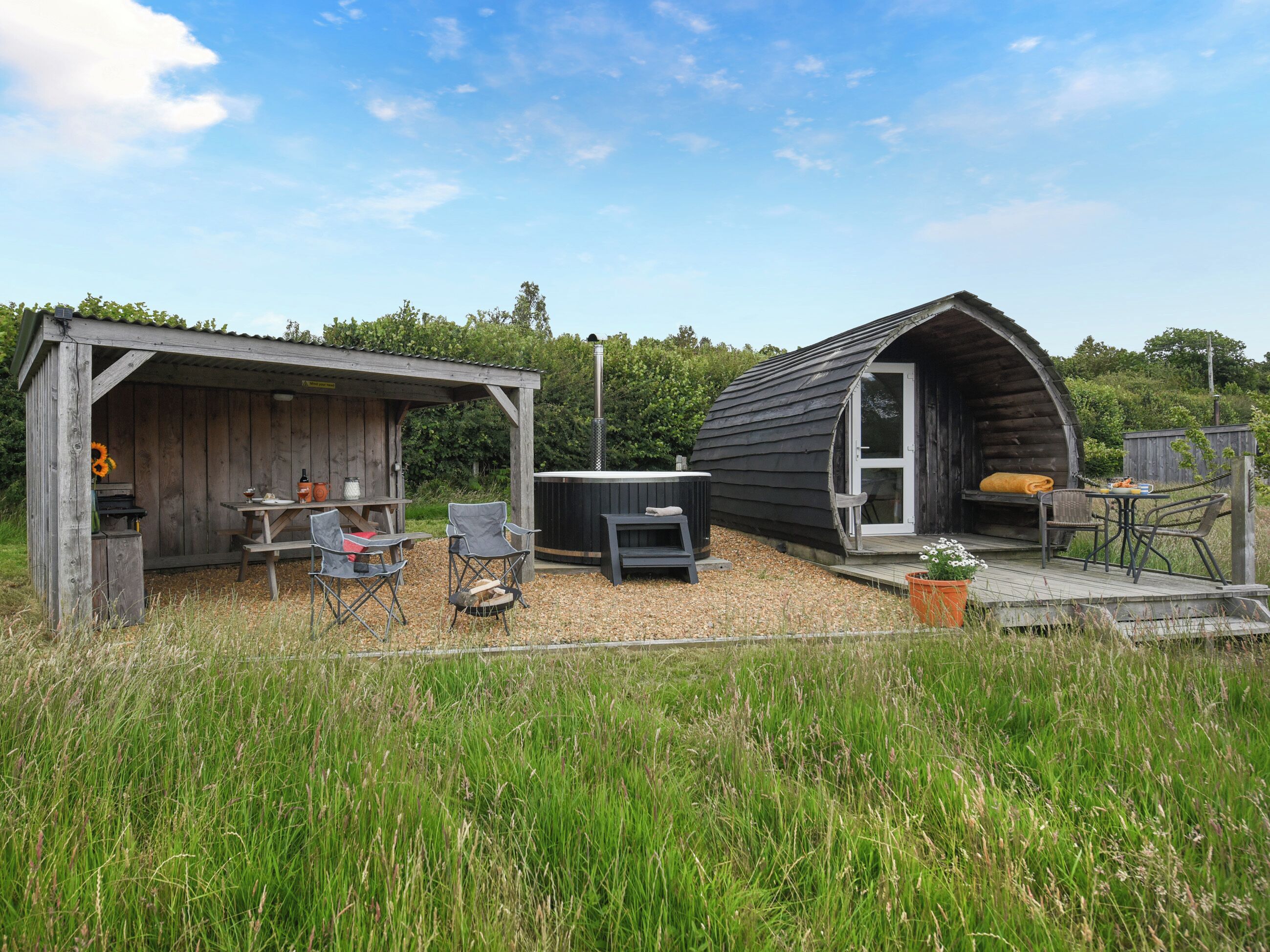 A rustic outdoor setting with a wooden structure featuring a covered patio area with seating and a hot tub.