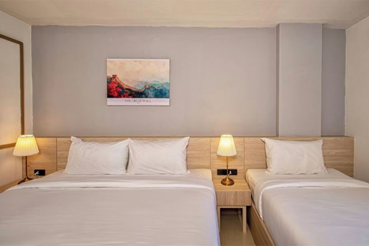 Habitación de hotel con dos camas, cabeceros, lámparas de noche, un cuadro colgado en la pared y mesitas de noche.