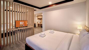 A hotel room with a bed, a TV on a wooden partition, a wardrobe, and a bathroom visible in the background.