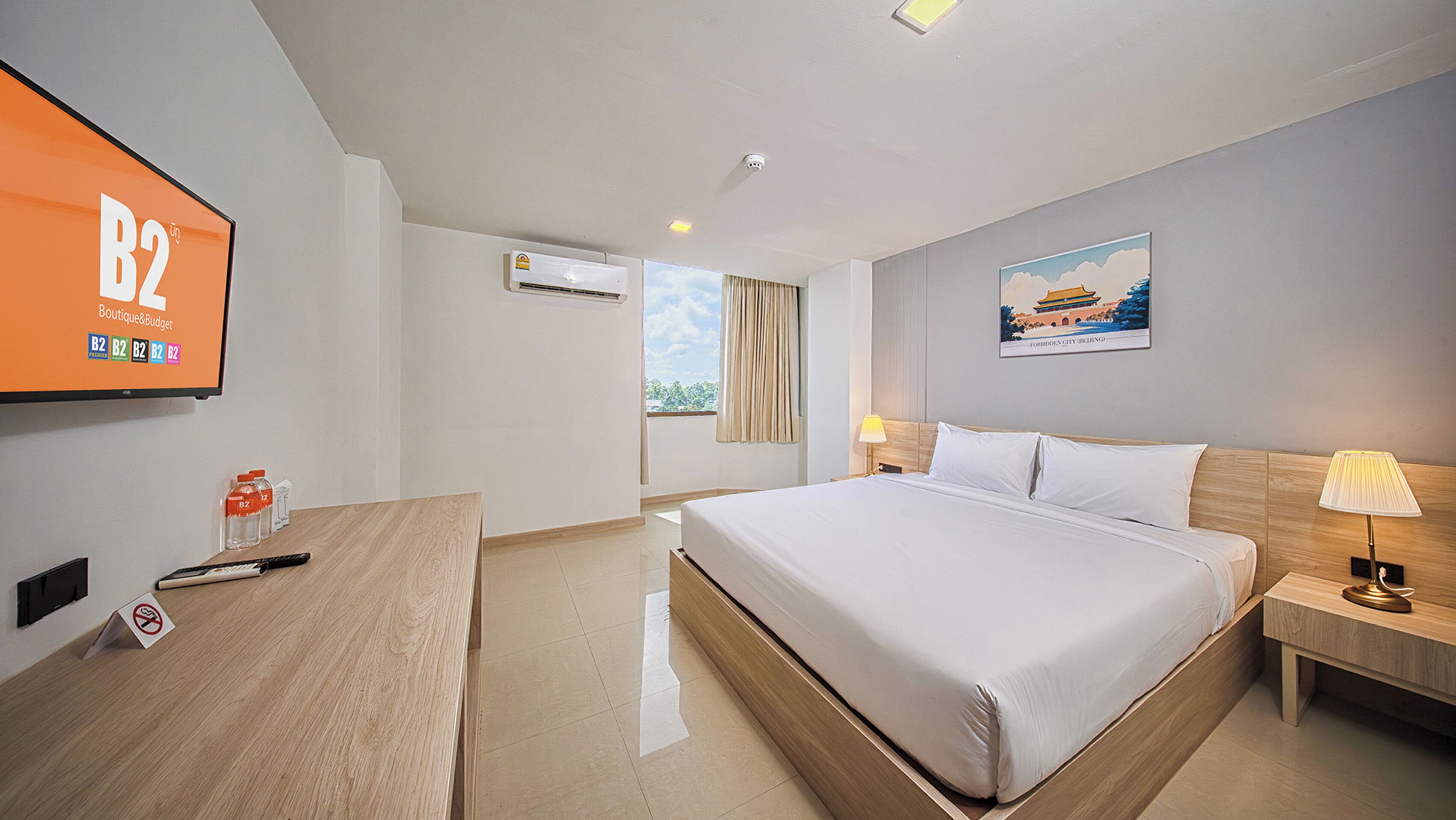 Quarto de hotel com uma cama grande, mesas de cabeceira, uma escrivaninha, uma televisão e um ar condicionado, além de um quadro na parede.