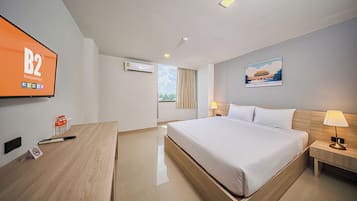 Quarto de hotel com uma cama grande, mesas de cabeceira, uma escrivaninha, uma televisão e um ar condicionado, além de um quadro na parede.
