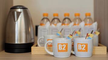 Una kitchenette con cafetera, dos tazas con el logotipo de 'B2 Boutique&Budget' y varias botellas de agua.