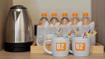 Una kitchenette con cafetera, dos tazas con el logotipo de 'B2 Boutique&Budget' y varias botellas de agua.
