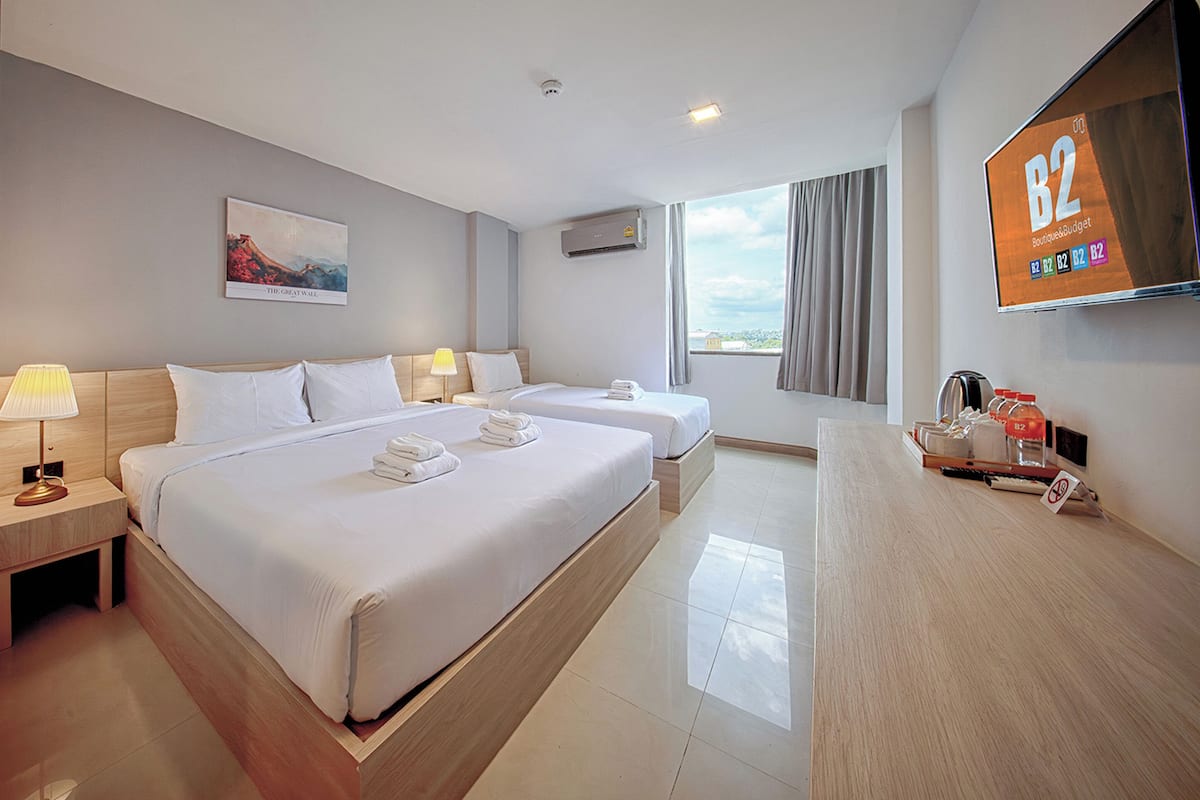 A hotel room with two beds, a flat-screen TV, a painting, and a view of the city.