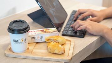 A laptop, a coffee cup, and a box of pastries on a wooden table.