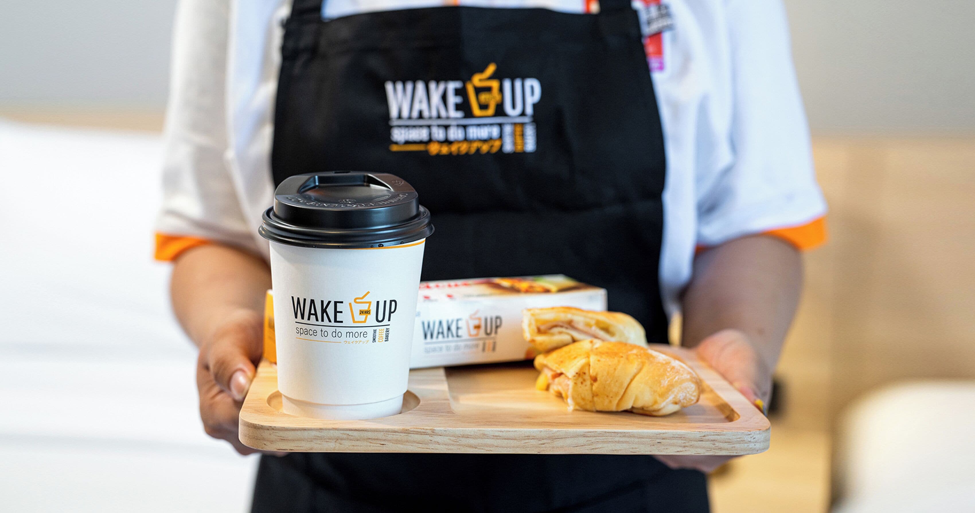 Una persona sosteniendo una bandeja con una taza de café y un sándwich.