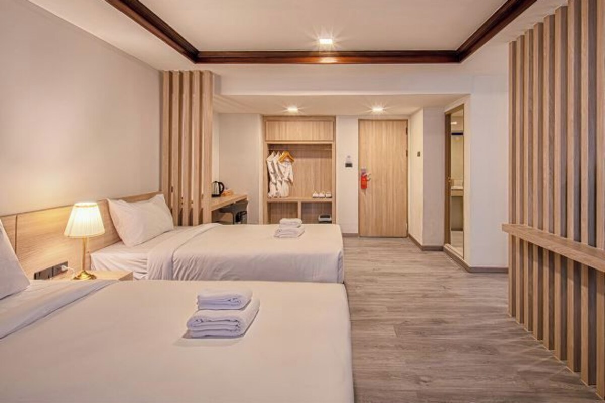 Una habitación de hotel con dos camas, un armario de madera, un espejo y una mesita de noche con una lámpara.