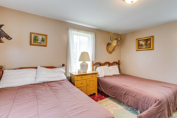 Una camera da letto con due letti, un comodino in legno, una lampada, una testa di cervo appesa al muro e due quadri incorniciati.