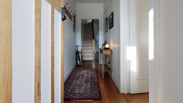 A hallway with a wooden floor, a patterned rug, a coat rack, and a staircase in the background. - Timeless Charm in the Heart of Launceston (Launceston)