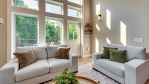 A spacious living room with two grey sofas, a coffee table, and large windows offering a view of the outdoors. - Burke Mtn | Slopeside | Bike Park & Trails Access (Burke)