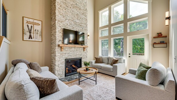 A living room with a stone fireplace, a flat-screen TV, and two sofas. - Burke Mtn | Slopeside | Bike Park & Trails Access (Burke)