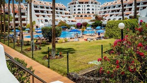 Un resort con varias construcciones blancas, una piscina central y palmeras.