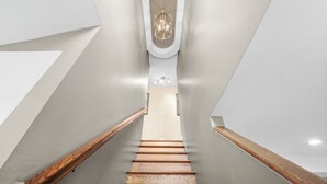 Una escalera moderna con escalones de madera y paredes blancas, que conduce a un techo con una lámpara.