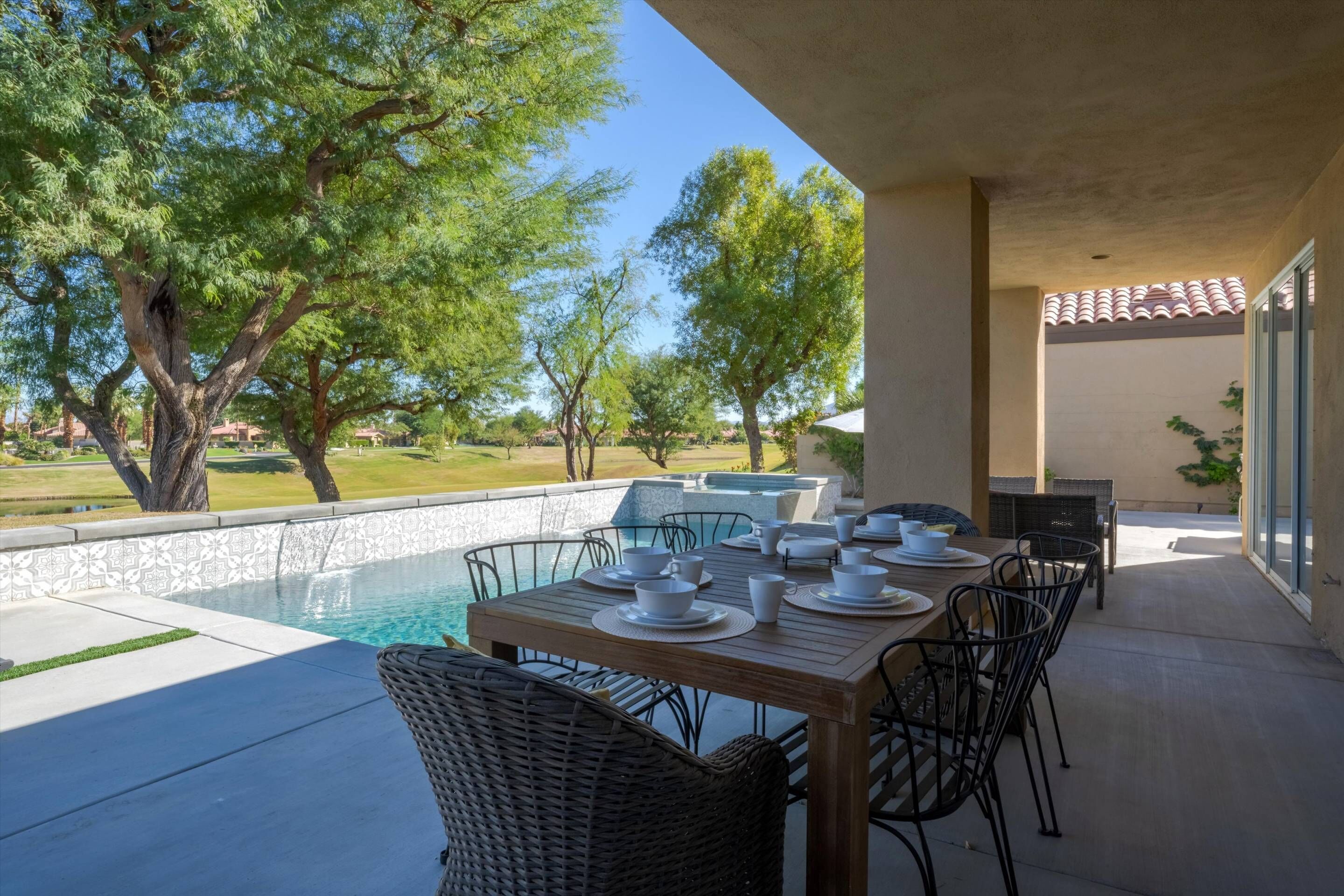 A dining area with a pool, outdoor furniture, and a view of trees and a swimming pool.