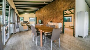 Ein modernes Interieur mit Holzbalkendecke, einem Essbereich mit Holztisch und Korbstühlen sowie Blick durch eine Glastür in einen Außenbereich.