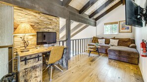 Ein gemütliches Zimmer mit einem hölzernen Schreibtisch, einem bequemen Sofa und einem an der Wand befestigten Fernseher.
