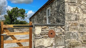 Un bâtiment en pierre doté d’un portail en bois, d’une fenêtre et d’un mur en pierre percé d’une ouverture circulaire.