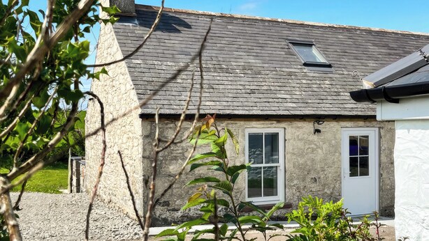 Une maison en pierre avec un toit en pente, une cheminée et une petite fenêtre.