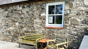 Un bâtiment en pierre avec une fenêtre, deux bancs en bois et une petite table.