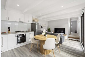 Una cocina moderna con armarios blancos, horno integrado y comedor con mesa redonda de madera y sillas blancas.