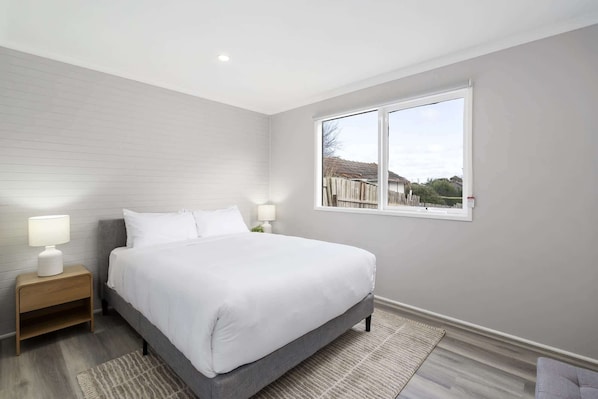 Un dormitorio con cama, dos mesitas de noche, ventana y vistas al exterior.