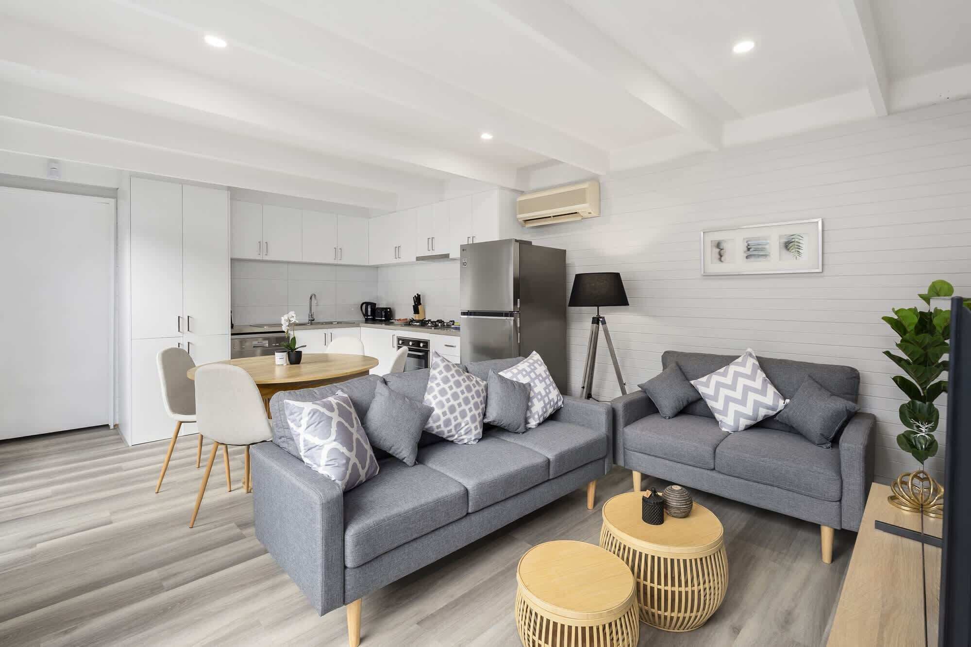 A modern living room with a grey sofa, two round wooden side tables, and a dining area with a wooden table and chairs.