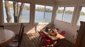 Ein überdachter Essbereich im Freien mit Tisch und Stühlen, große Fenster mit Seeblick und eine Holzterrasse.