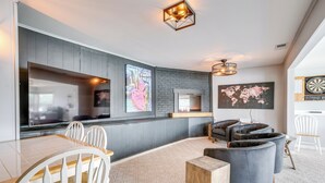 Ein modernes Wohnzimmer mit großem Fernseher, bequemen Sitzmöglichkeiten, Kamin und Dartscheibe.