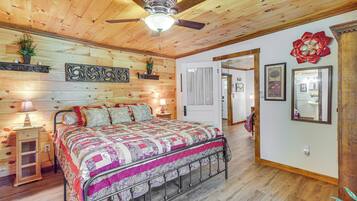 A bedroom with a wooden ceiling, a bed with a patterned bedspread, a nightstand with a lamp, and a wall with decorative items.