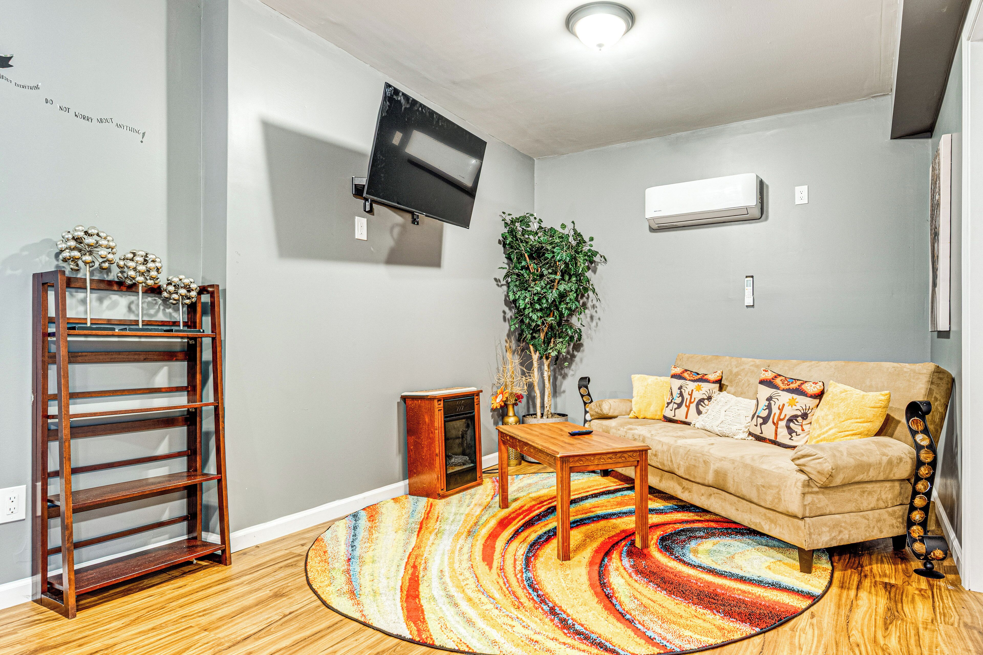 A living room with a sofa, a coffee table, a wooden bookshelf, a TV mounted on the wall, and an air conditioning unit.