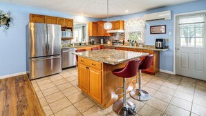A modern kitchen with wooden cabinets, stainless steel appliances, a granite countertop, and a bar area with stools.