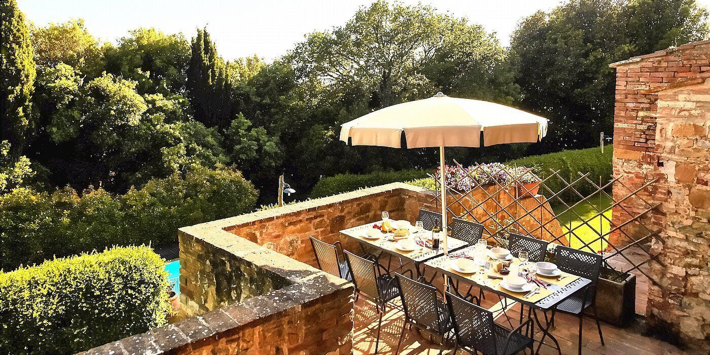 An outdoor dining area with a table set for four, surrounded by stone walls and a large umbrella.